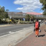Woman walking down brick paved sidewalk with pedestrian bridge in distance.